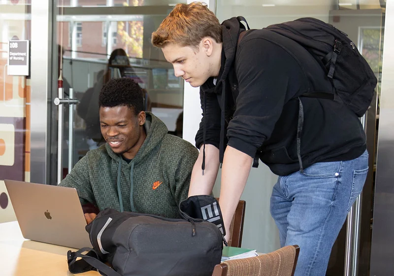 Two students collaborating at a laptop in a university setting, sharing ideas and working together.