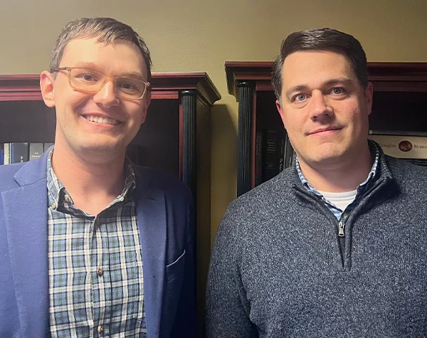 Two men smiling for a photo, standing side by side in an office setting.