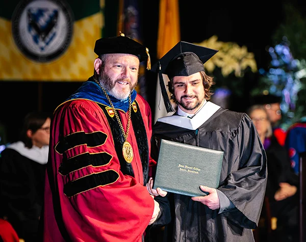 A graduate receives their diploma during a commencement ceremony, highlighting the moment of achievement and celebration.