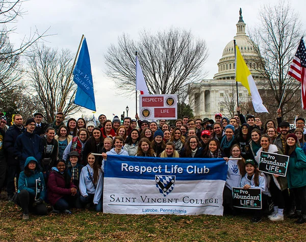 A large group of students from Saint Vincent College, holding a Respect Life Club banner, gathers in front of the U.S. Capitol building during a pro-life event.