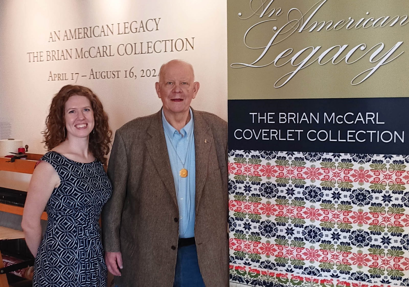 A woman and man pose together next to a display sign for "An American Legacy: The Brian McCarl Collection" exhibition.