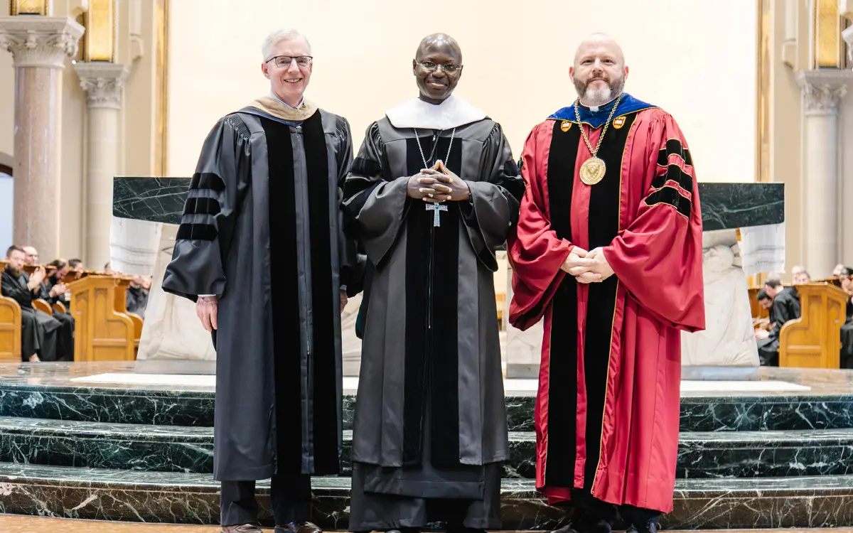 Three university leaders in academic regalia, including a dean and a president, pose together during a ceremony.