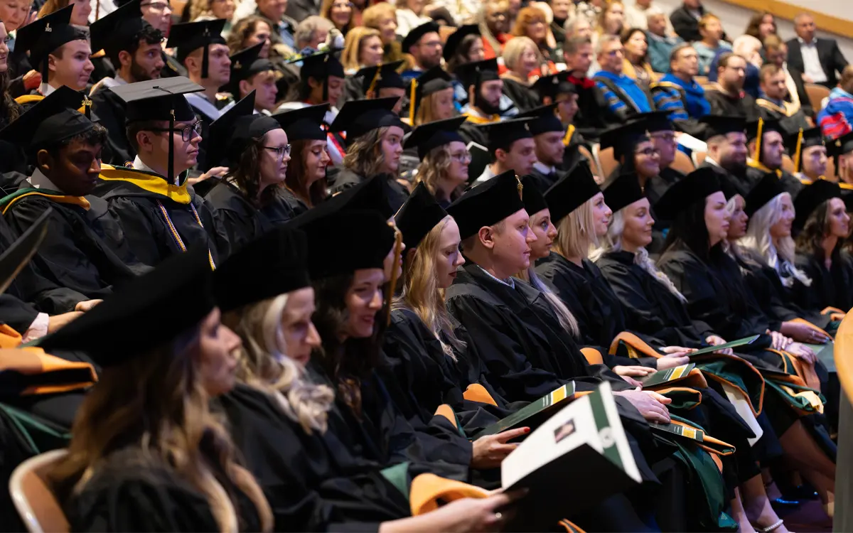 A crowded graduation ceremony featuring graduates in black caps and gowns, focused on their diplomas.