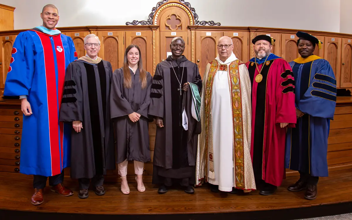 A group of seven individuals in academic regalia, including faculty members and a graduate, posing together in a ceremonial setting.