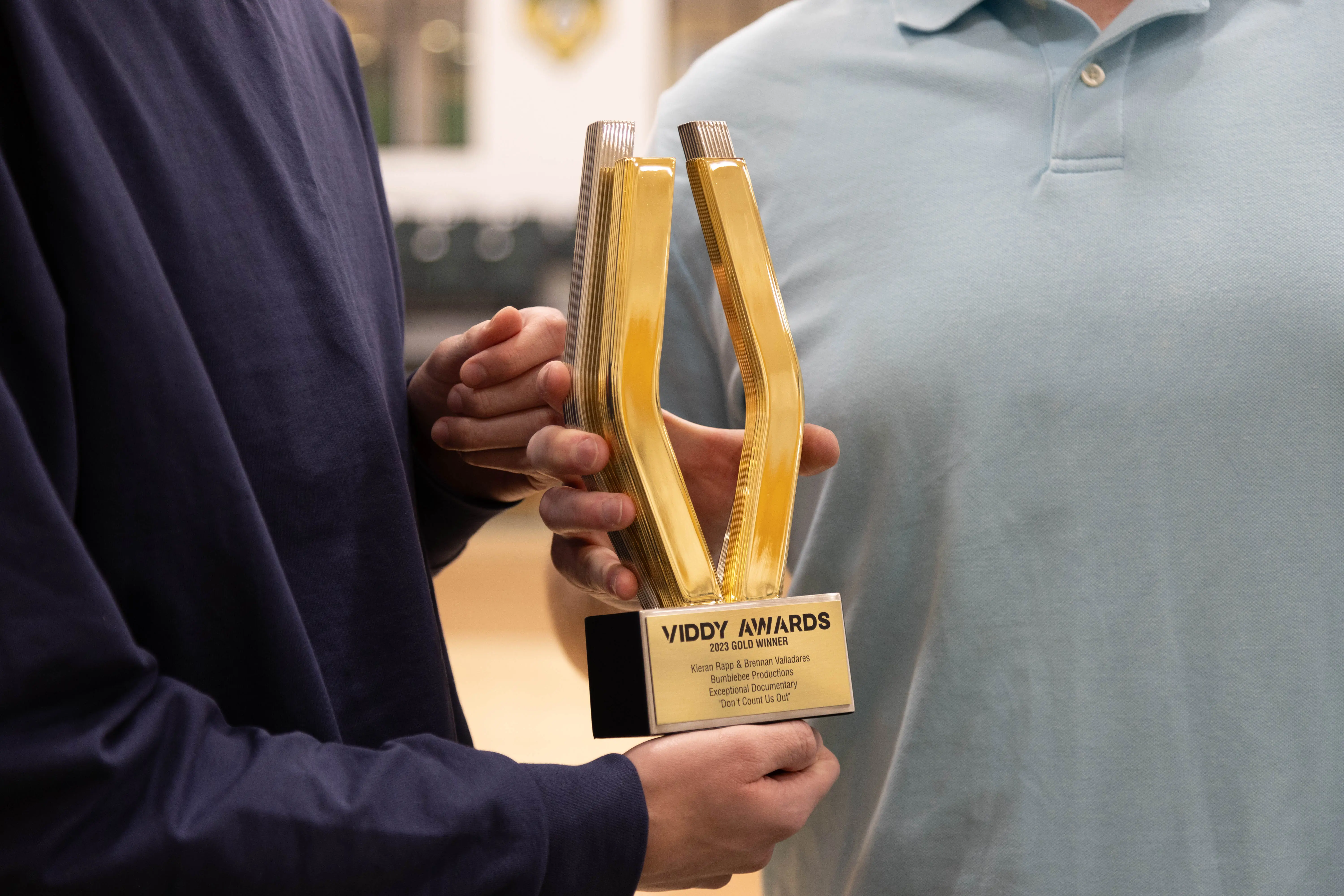 Two individuals holding a golden trophy shaped like a pair of clippers, awarded at the Viddy Awards for excellence in video production.