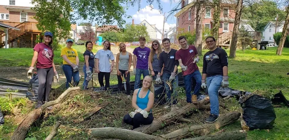 A group of volunteers poses together outdoors after completing a community cleanup project, surrounded by piles of debris and greenery.