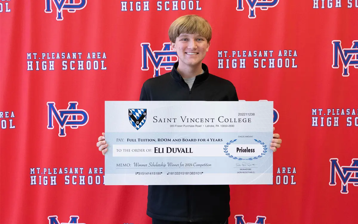 A student holds a scholarship announcement board from Saint Vincent College, celebrating full tuition, room, and board for four years.