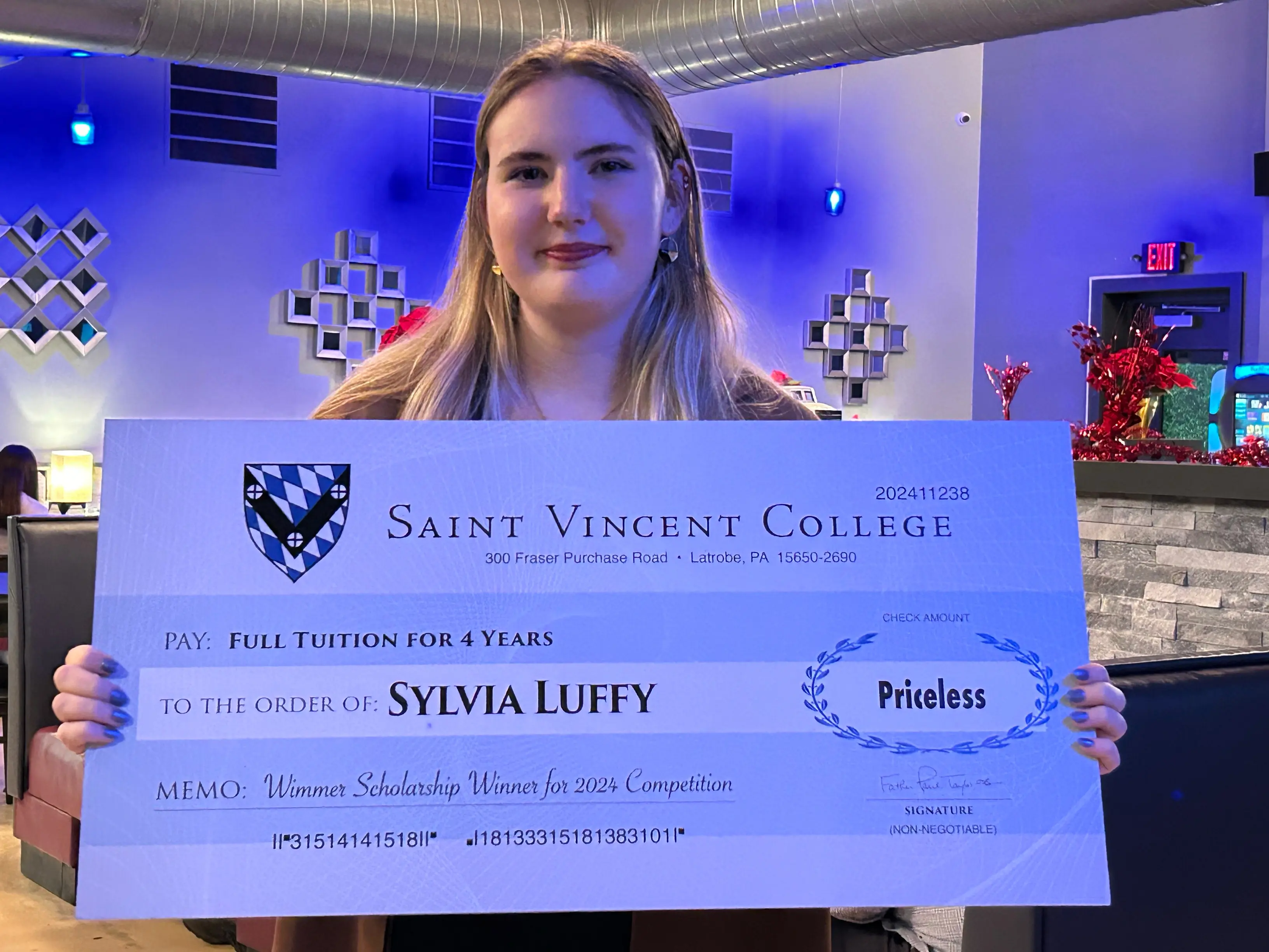 A young woman holding a large scholarship check from Saint Vincent College, awarded to her for winning the 2022 competition.