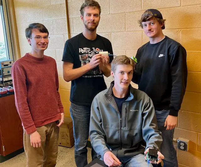 Group of four students working together on a robotics project, with one of them holding a component.