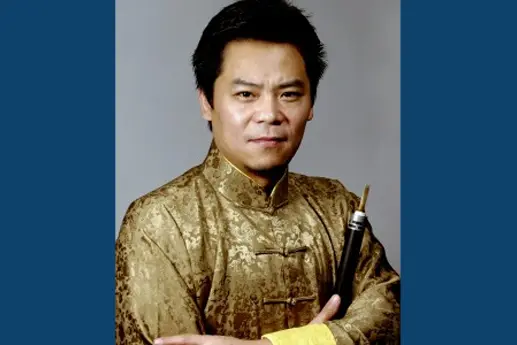 A man wearing a traditional gold-patterned Chinese outfit, confidently posing with a musical instrument.