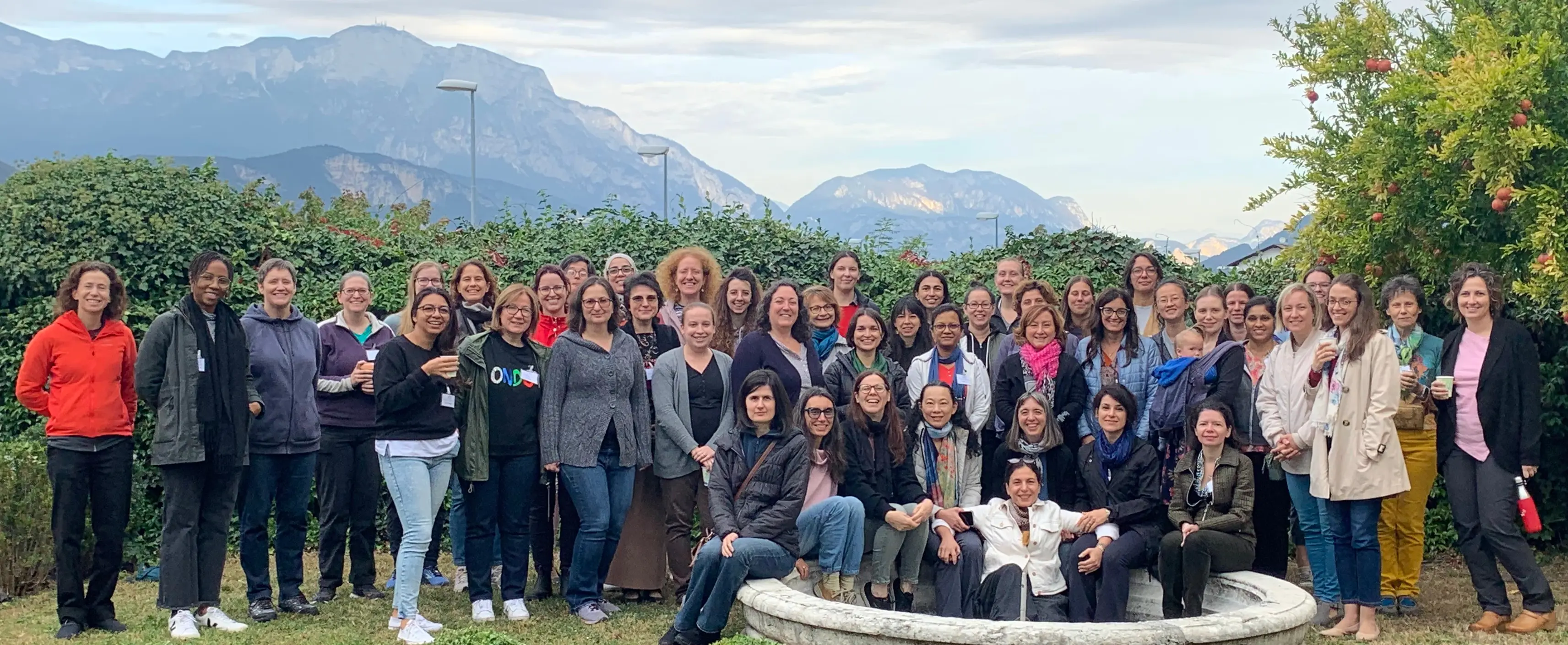 Group photo of diverse women gathered outdoors with mountains in the background.