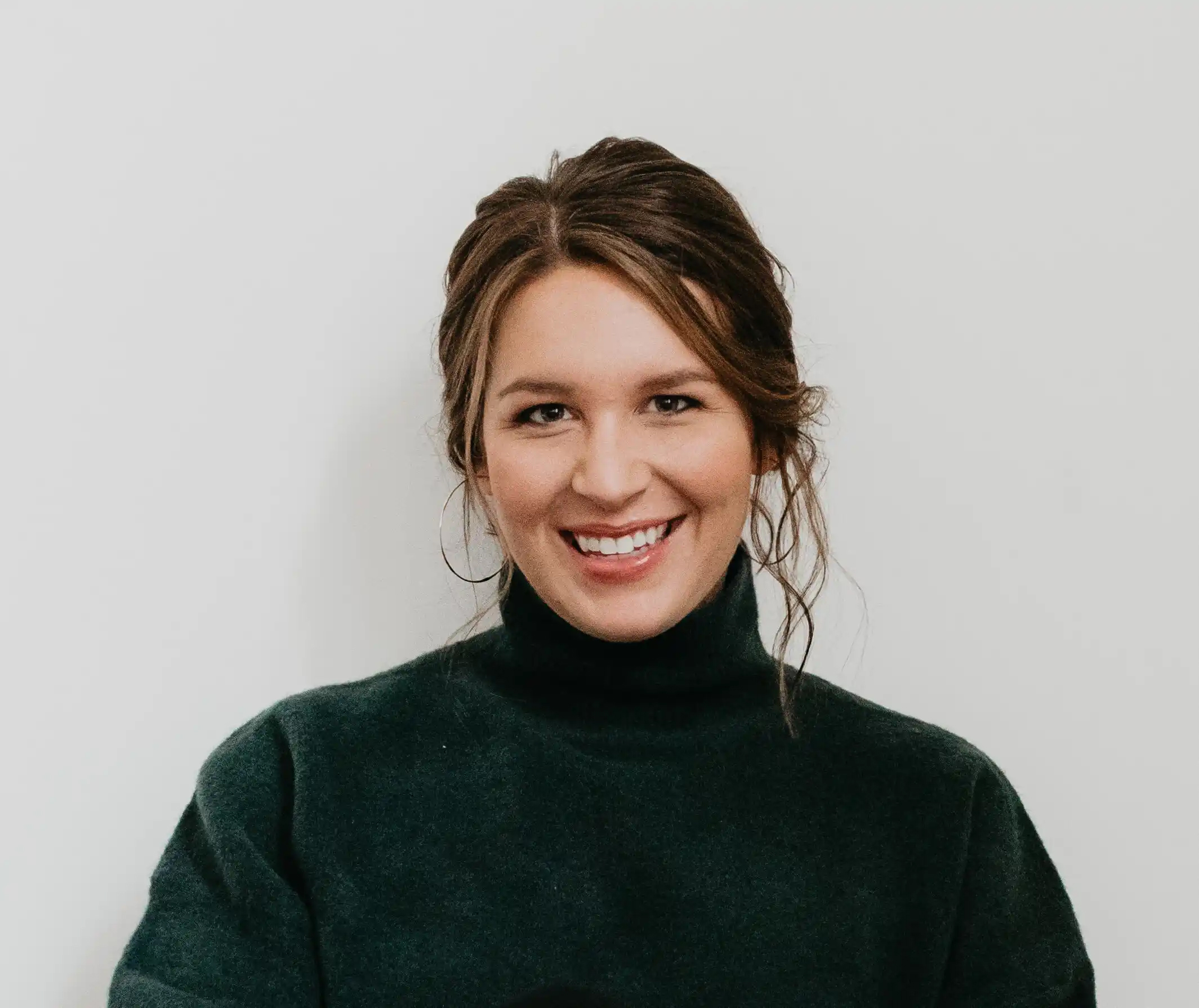 A smiling woman in a green turtleneck sweater poses against a plain background.