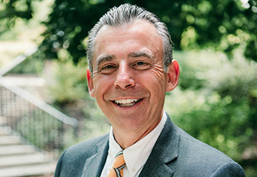 Dr. Todd Whitaker in a suit stands outdoors, surrounded by greenery.