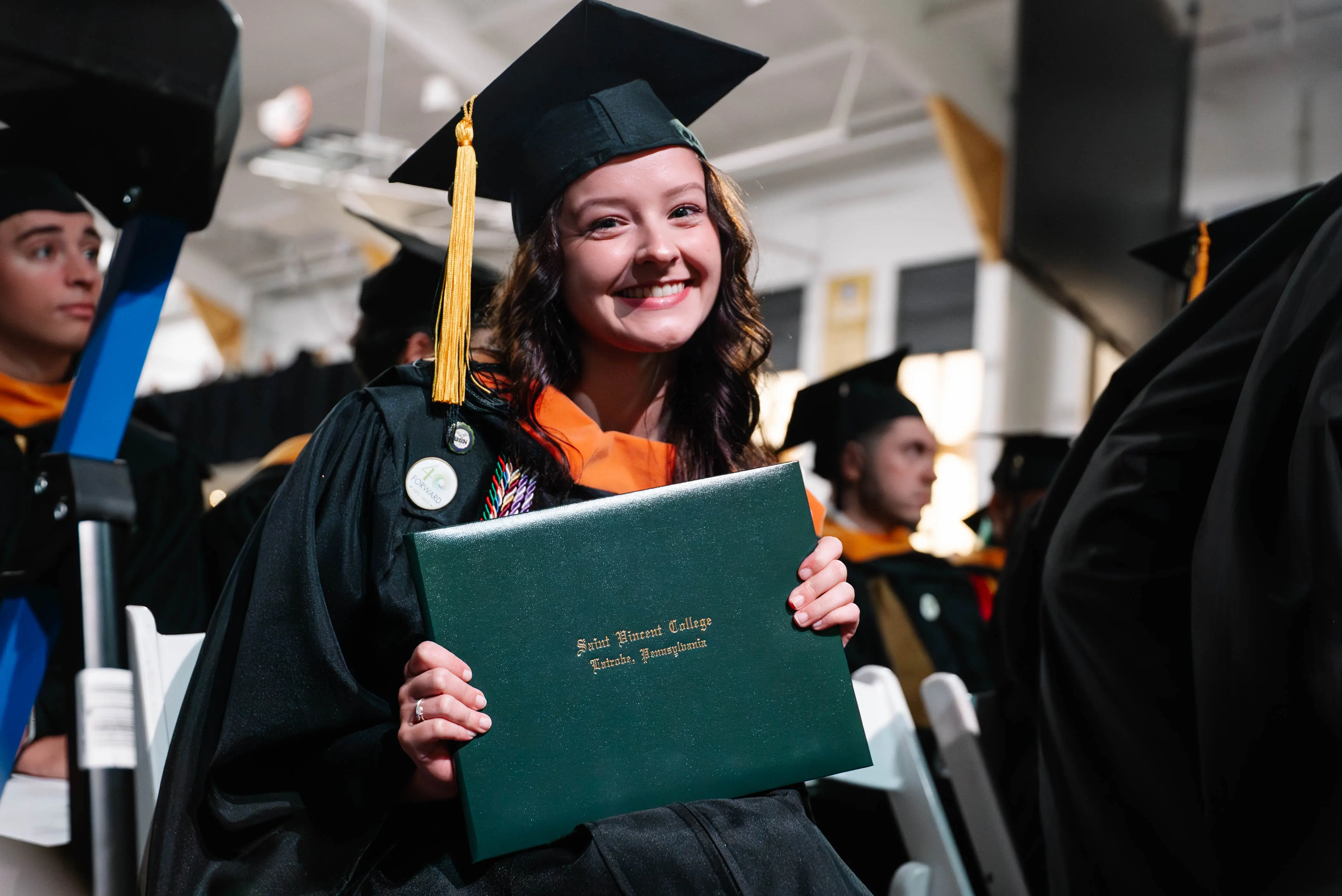 A smiling graduate in cap and gown holds her diploma from a college graduation ceremony.