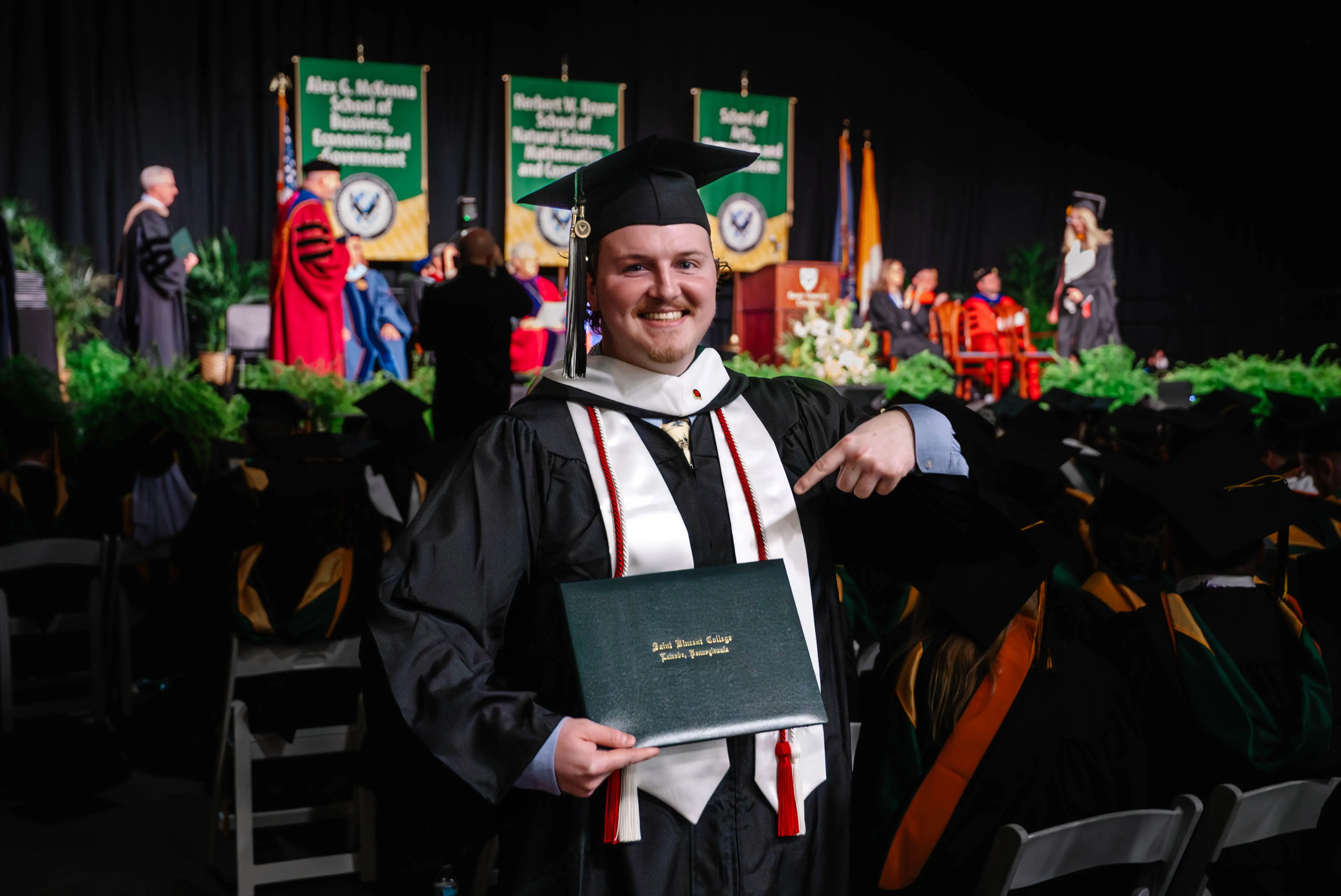 A graduate in cap and gown proudly holds up his diploma during a commencement ceremony.