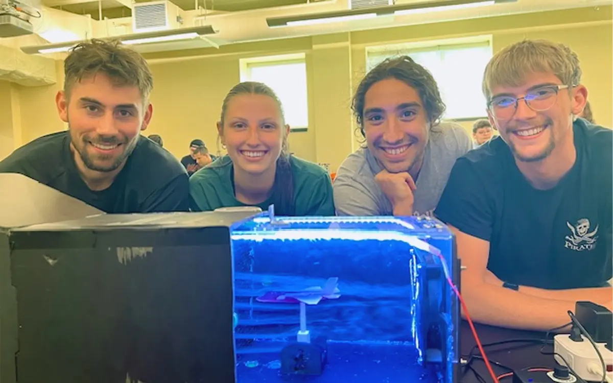 Four students pose with their aquatic project in a classroom, showcasing teamwork and innovation.