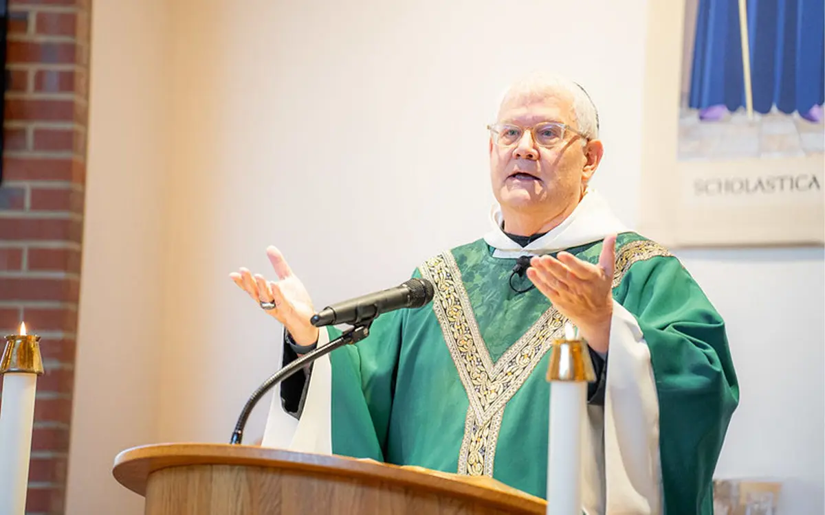 A priest delivering a sermon at the altar, wearing a green vestment with a gold trim.