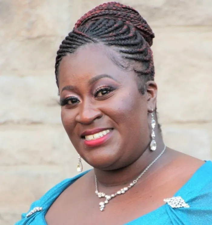 A smiling woman with braided hair, wearing elegant jewelry and a blue dress.