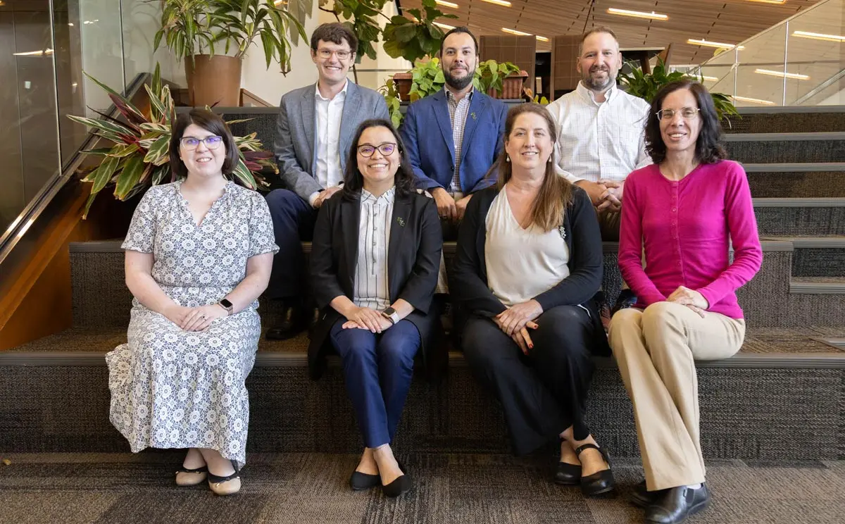 A group photo of eight professionals posing on stairs in an office environment, showcasing diversity and teamwork.