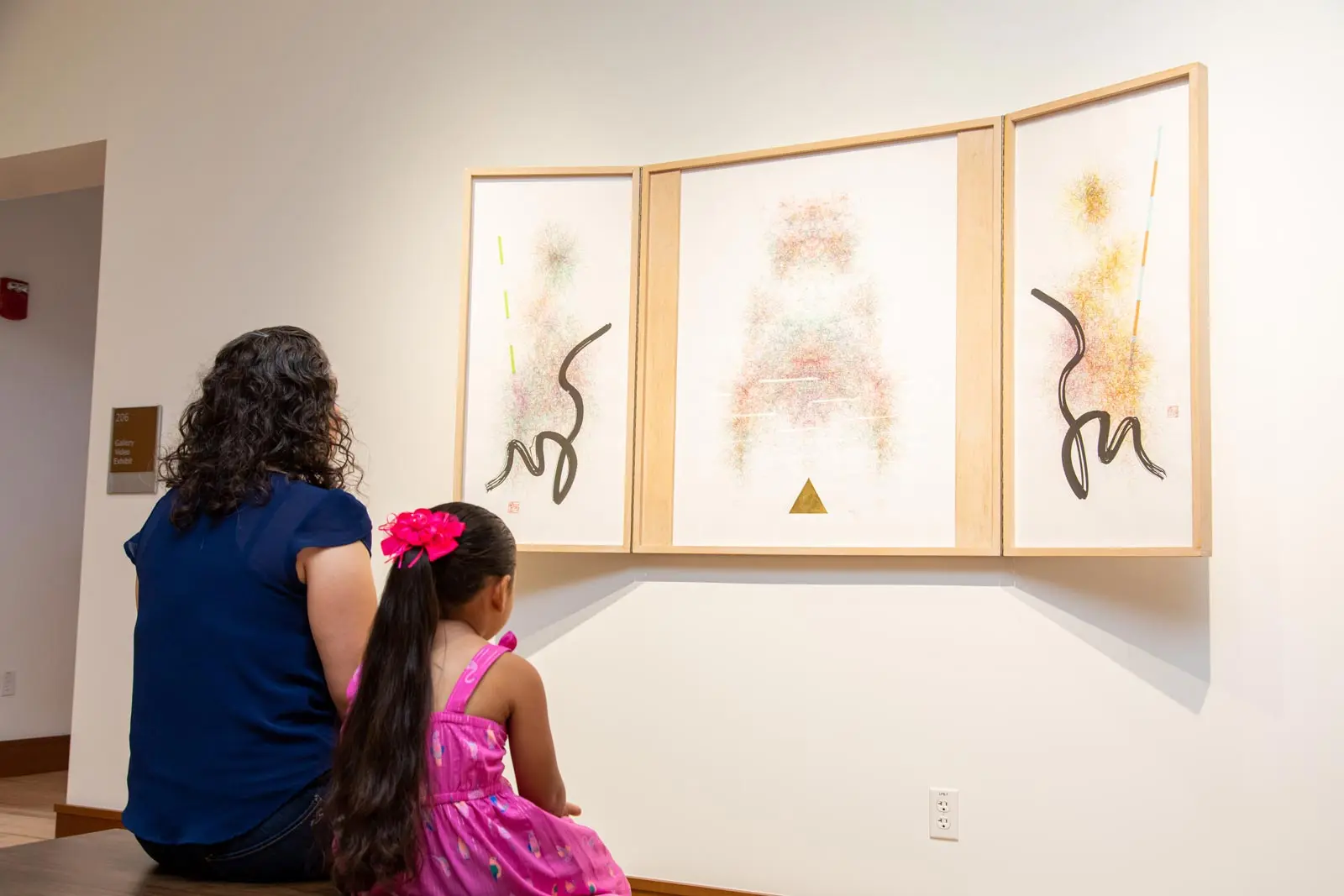 A mother and daughter admire a colorful abstract artwork displayed in a museum.