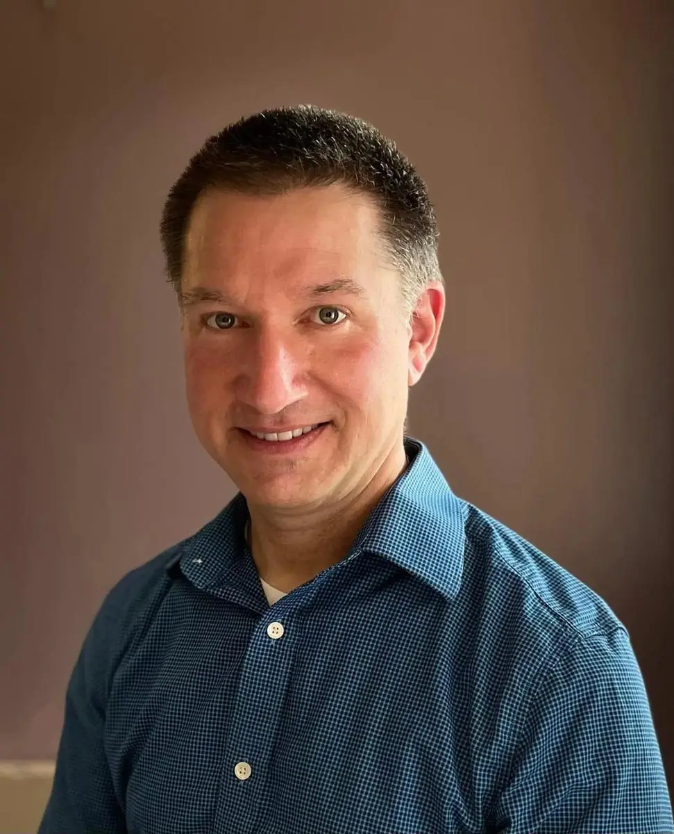 A friendly portrait of a man wearing a blue checkered shirt, smiling at the camera.