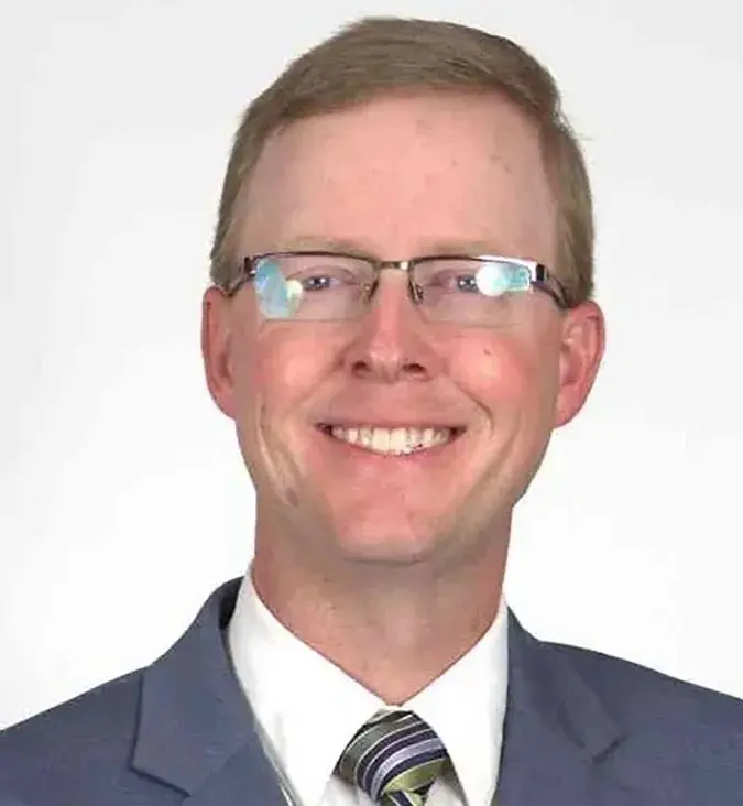 Professional headshot of a smiling man in a suit with glasses.