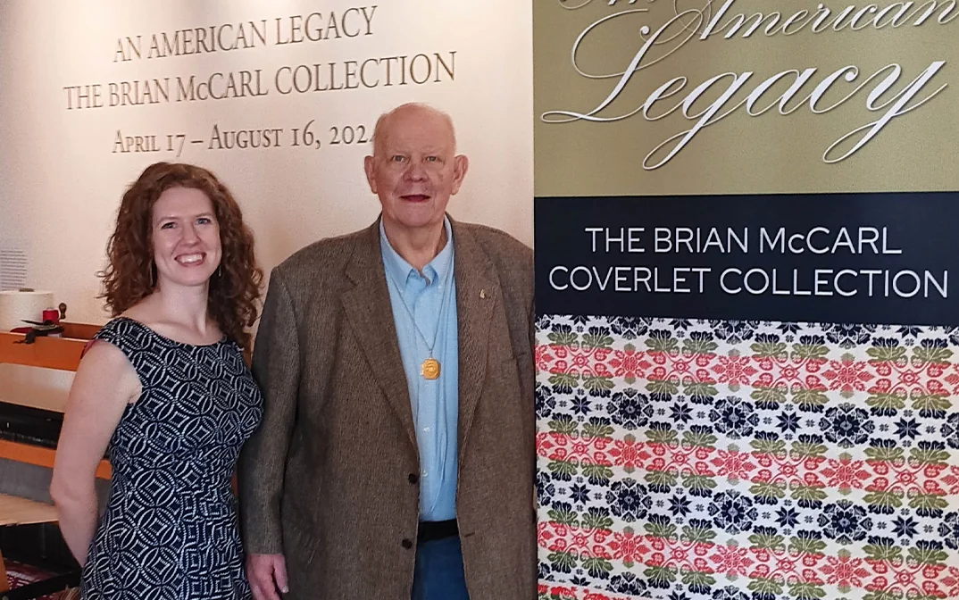 A woman and man pose together next to a display sign for "An American Legacy: The Brian McCarl Collection" exhibition.