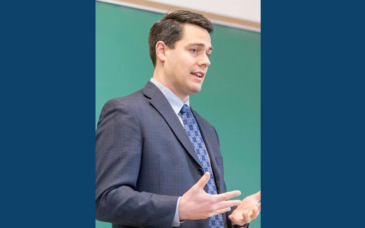 Dr. Jerome Foss gestures while speaking in front of a green chalkboard.