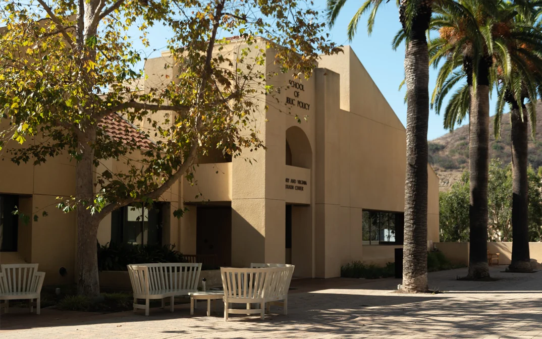 Exterior view of a Pepperdine University building with the sign "School of Public Policy," surrounded by palm trees and seating areas.