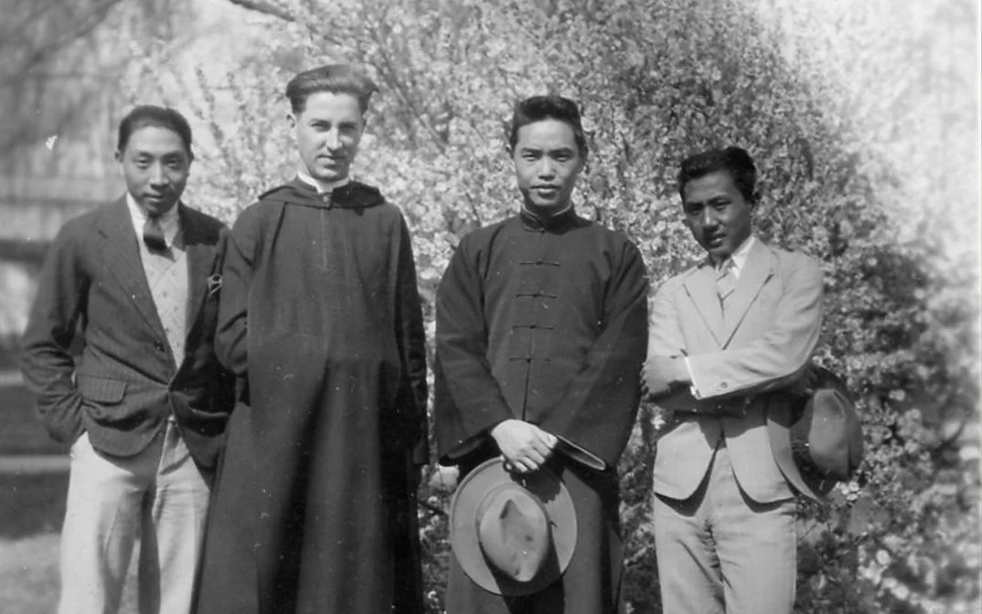 Historical photograph featuring four men in traditional and formal attire, standing outdoors in front of a flowering tree.